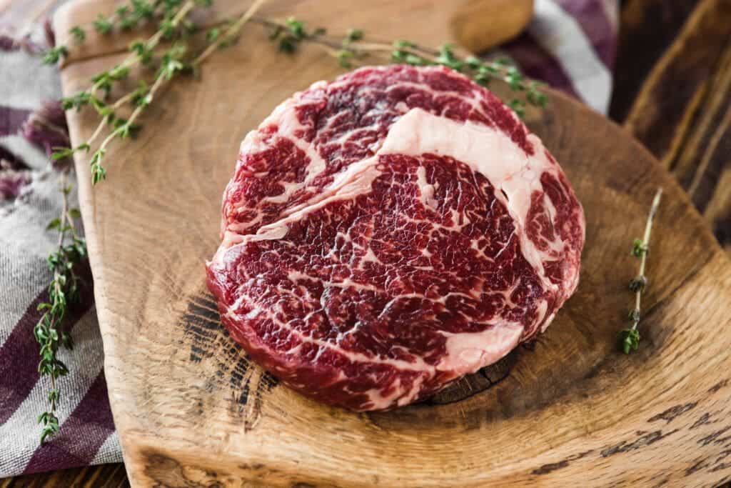 Ribeye maturé, grillé, accompagné de beurre aux herbes et à la truffe 2 Ribeye de bœuf Aurocha vieilli, viande de qualité supérieure, présenté sur une planche à découper en bois massif avec une belle marbrure