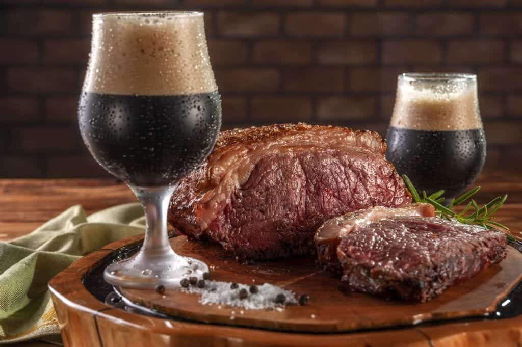 duas canecas de cerveja preta bem gelada, acompanhadas por uma picanha servida numa tábua de madeira natural